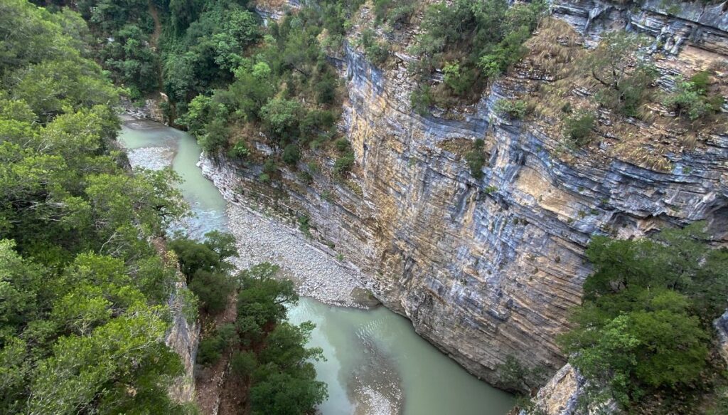 Aerial view of the walls of Osum Canyon and the light green river running through it with trees on either side.