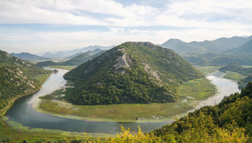 View of Skader Lake winding around a green mountain from Pavlova Strana Viewpoint in Montenegro. 
