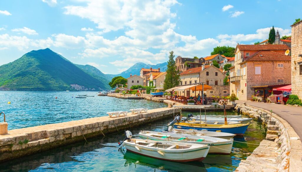View of a series of small row boats sitting in the water in Perast with stone buildings in the background.  