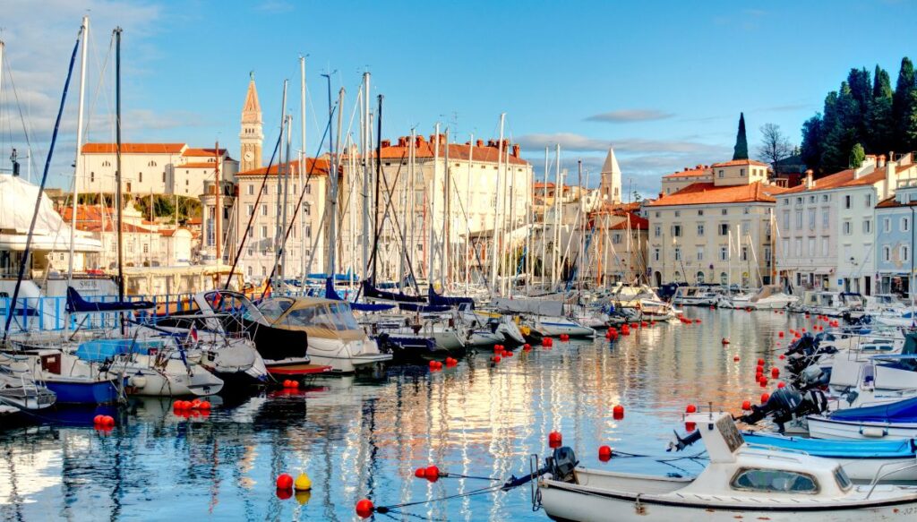 View of sailboats sitting in the harbor surrounded by charming white buildings in Piran, Slovenia.