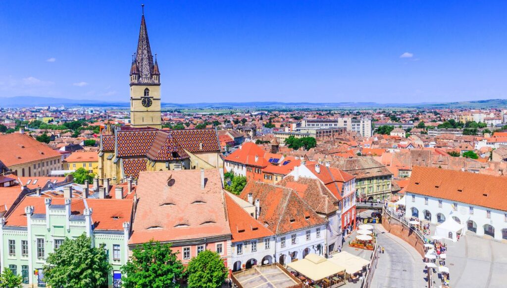 View of the Lutheran Church steeple and a town square lined with charming buildings on a sunny day in Sibiu.