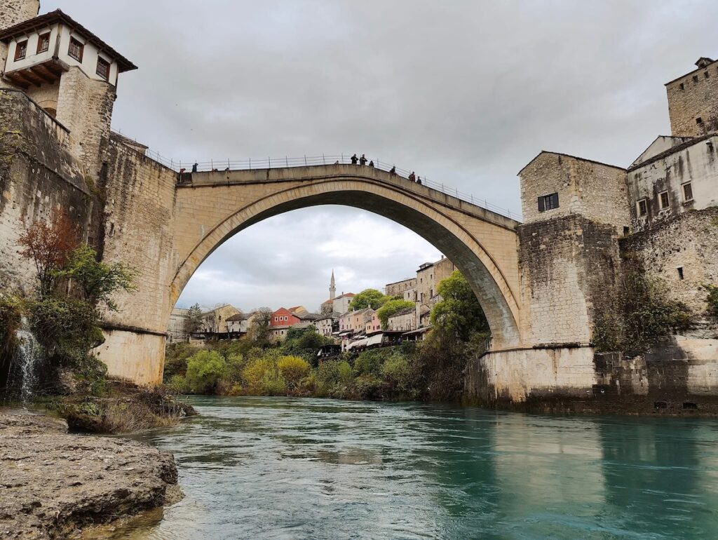 View of the Stari Most bridge from the bottom of the river looking up. You can see people looking down ar the river from the arched stone bridge.