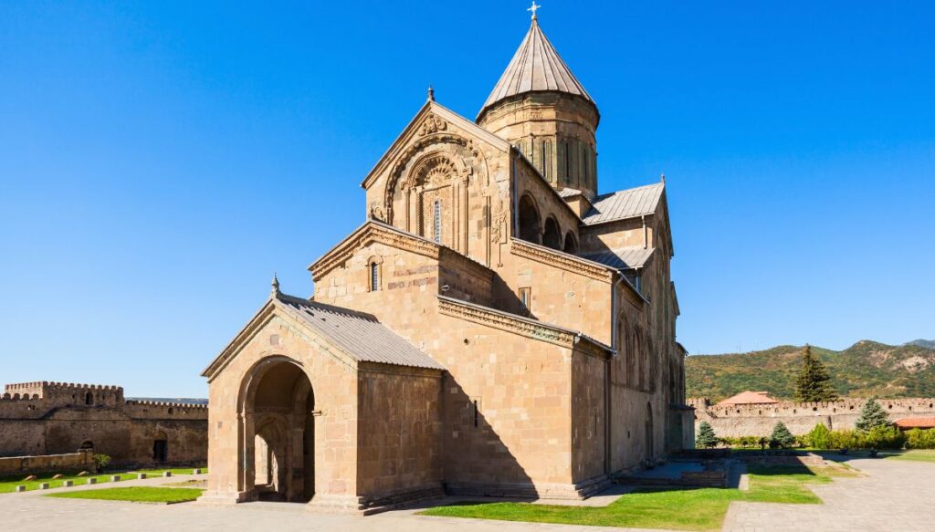 View of Svetitskhoveli Cathedral on a sunny day with stone wallas and a pointed roof. 