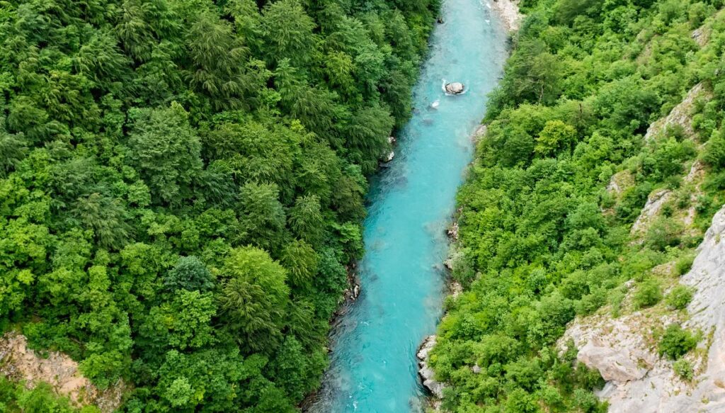 Aerial view of bright blue water running through Tare River Canyon with green trees on both sides of the river. 