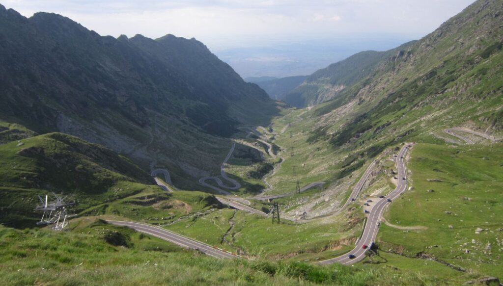 Aerial view of the switchbacks along Transfăgărășan with the green mountains all around the cars driving on the road.