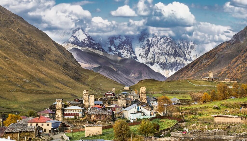 View of the town of Ushguli sitting in the middle of a valley with snow covered mountains in the background in Georgia. 