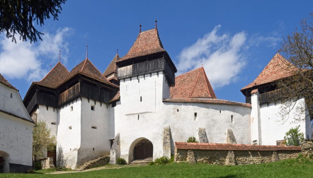 View of a white fortified church with a reed roof and turets in Viscri.