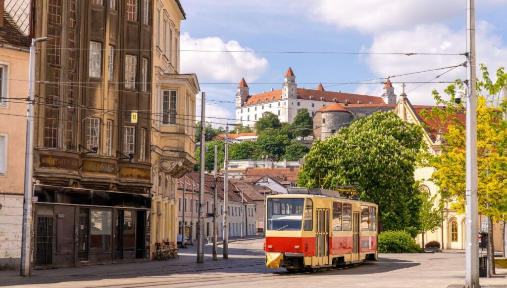 View of an old yellow tram running through the streets of Bratislava with the white castle on a hill in the background in one of the most beautiful places in Slovakia.
