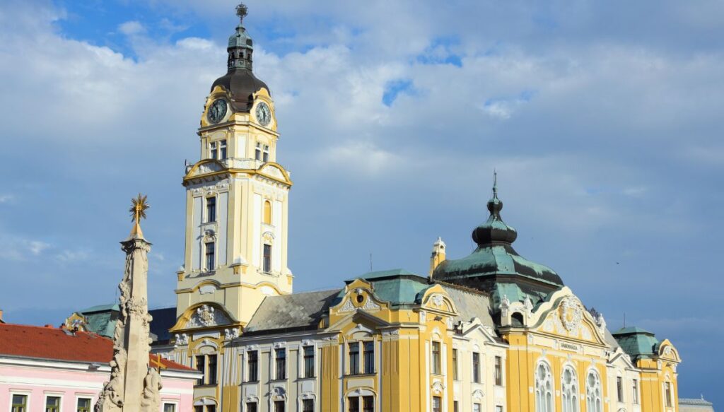 View of historic yellow and white historic building with a steeple in the center of Pecs, Hungary.